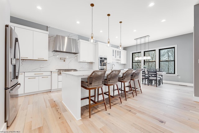 kitchen with a center island with sink, wall chimney range hood, white cabinetry, and appliances with stainless steel finishes