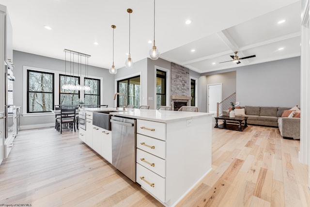 kitchen featuring dishwasher, a kitchen island with sink, beamed ceiling, white cabinetry, and decorative light fixtures