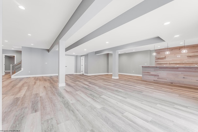 basement featuring bar area, light hardwood / wood-style floors, and wooden walls