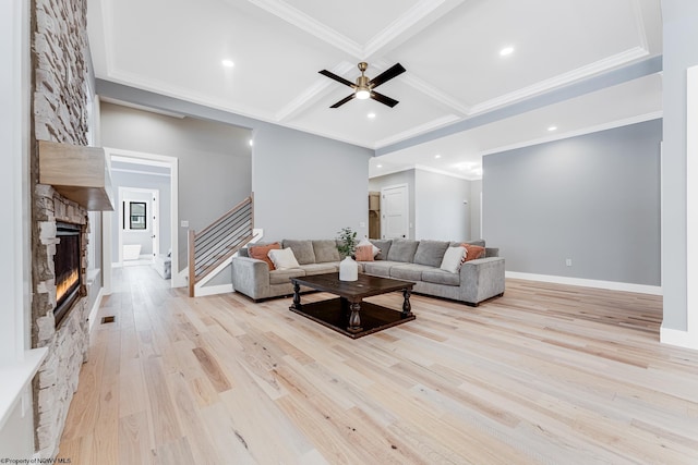 living room featuring light hardwood / wood-style flooring, crown molding, ceiling fan, coffered ceiling, and a stone fireplace