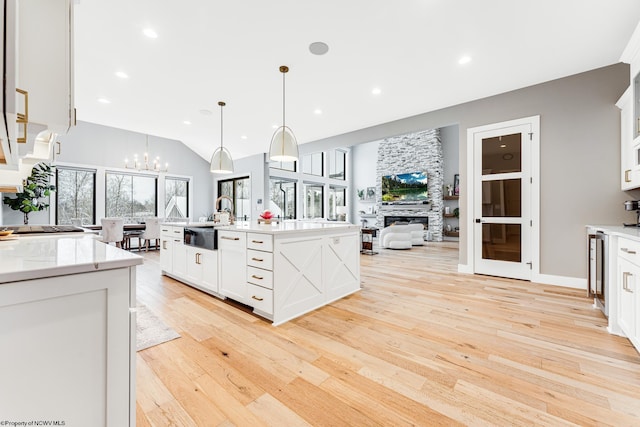 kitchen featuring light hardwood / wood-style flooring, decorative light fixtures, a kitchen island with sink, white cabinetry, and a fireplace