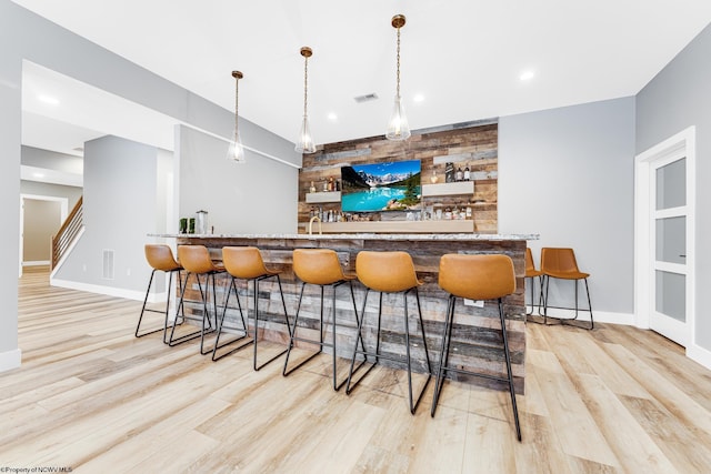 bar with hanging light fixtures and light wood-type flooring