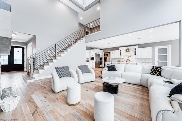 living room featuring crown molding, light wood-type flooring, french doors, and a towering ceiling