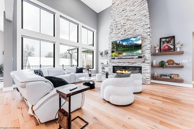 living room featuring light wood-type flooring, a towering ceiling, and a fireplace