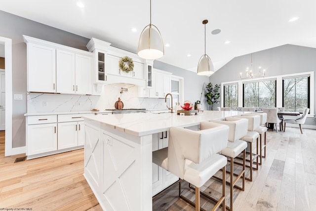 kitchen with white cabinets, an island with sink, and lofted ceiling