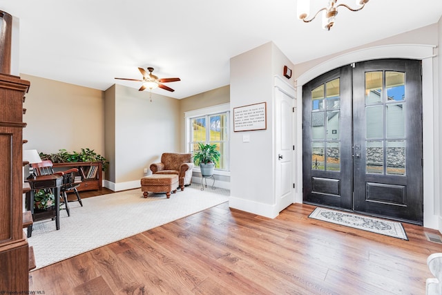 foyer with ceiling fan with notable chandelier, french doors, and light wood-type flooring