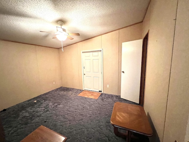 spare room with a textured ceiling, dark colored carpet, ceiling fan, and crown molding