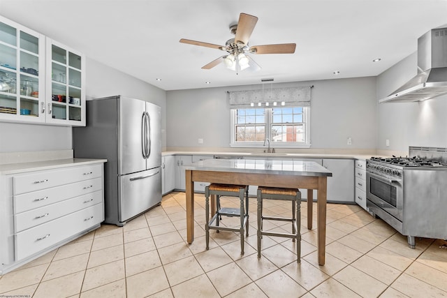 kitchen with appliances with stainless steel finishes, light tile patterned floors, wall chimney exhaust hood, white cabinets, and sink