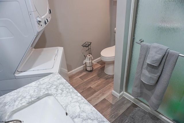 bathroom with toilet, vanity, a shower with shower door, and stacked washer / dryer