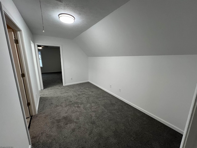 bonus room featuring a textured ceiling, vaulted ceiling, and dark colored carpet