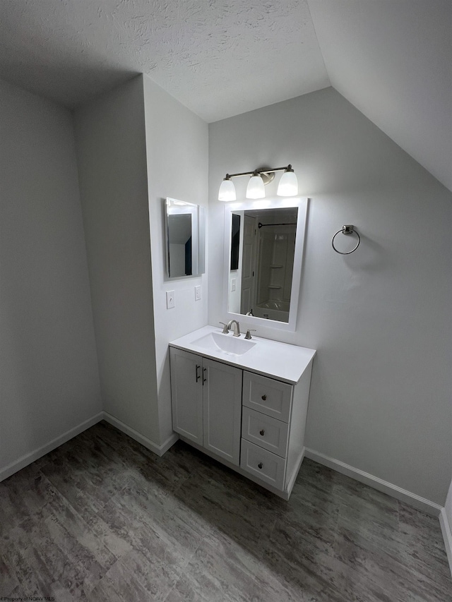 bathroom featuring wood-type flooring, vanity, lofted ceiling, and a textured ceiling