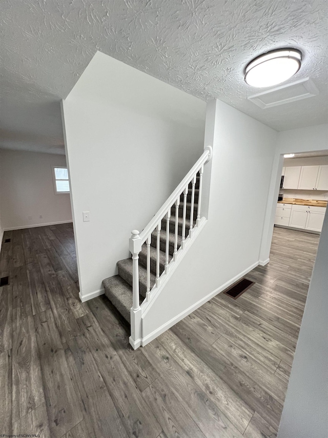 staircase with hardwood / wood-style floors and a textured ceiling