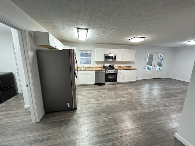 kitchen with white cabinets, appliances with stainless steel finishes, a textured ceiling, and dark hardwood / wood-style floors