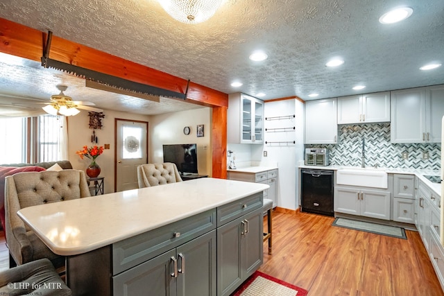 kitchen with a breakfast bar, gray cabinetry, open floor plan, a sink, and light wood-type flooring