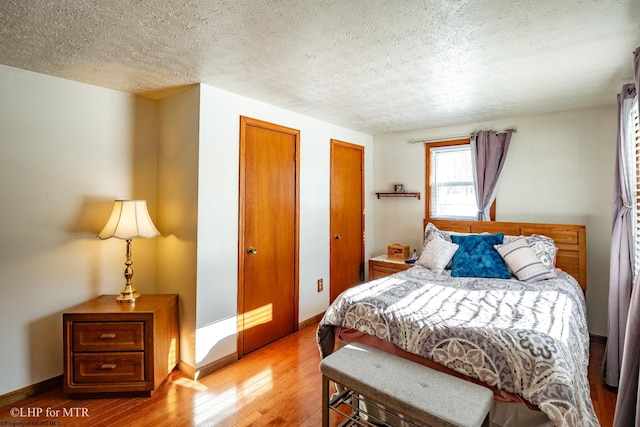 bedroom featuring wood-type flooring, a textured ceiling, and two closets