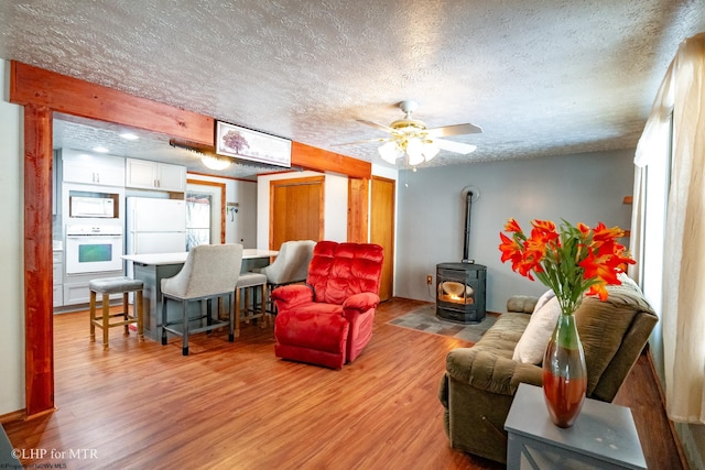 living room with a ceiling fan, a wood stove, a textured ceiling, and light wood finished floors