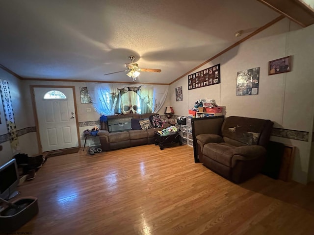 living room featuring ceiling fan, vaulted ceiling, wood-type flooring, ornamental molding, and a textured ceiling