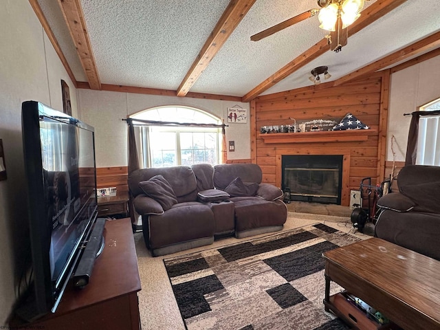 carpeted living room with a textured ceiling, ceiling fan, wood walls, and beamed ceiling