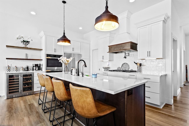 kitchen with decorative light fixtures, backsplash, premium range hood, white cabinetry, and beverage cooler