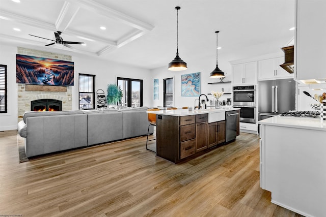 kitchen with white cabinetry, light hardwood / wood-style floors, coffered ceiling, an island with sink, and hanging light fixtures