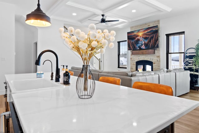 dining area featuring coffered ceiling, ceiling fan, a fireplace, beam ceiling, and sink