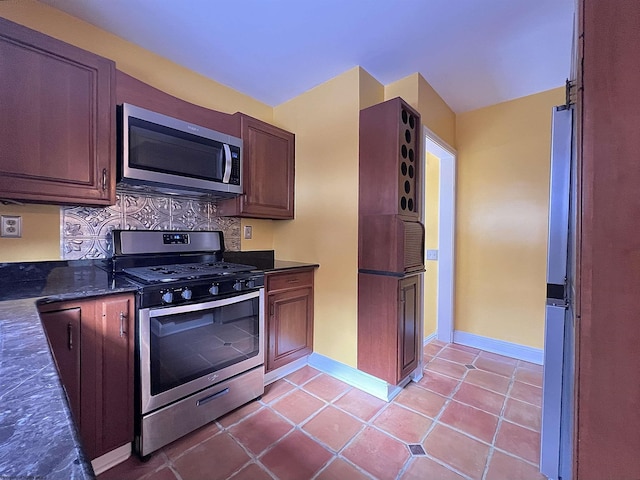 kitchen featuring light tile patterned floors, backsplash, appliances with stainless steel finishes, and dark stone counters