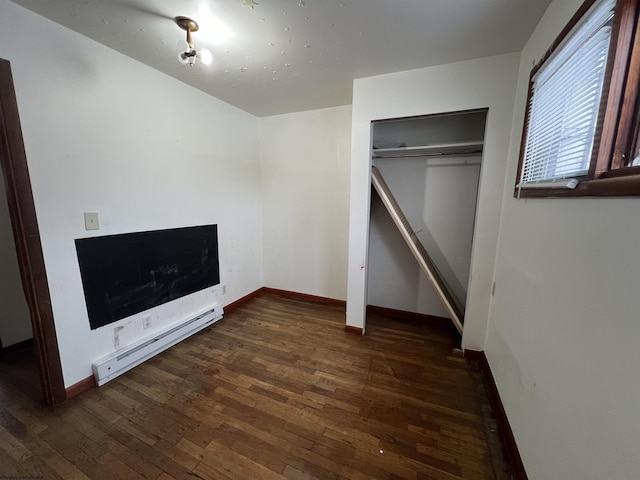 unfurnished bedroom featuring baseboard heating, a closet, and dark hardwood / wood-style floors