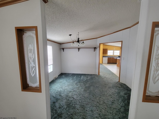 carpeted spare room with a textured ceiling, ornamental molding, a notable chandelier, and vaulted ceiling