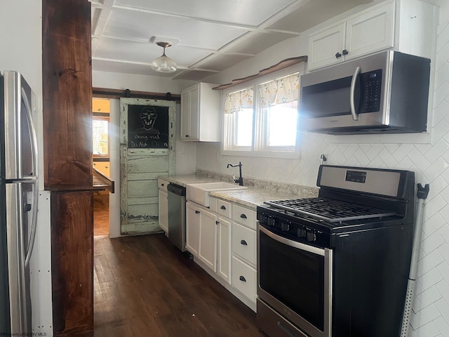 kitchen featuring white cabinetry, dark hardwood / wood-style flooring, stainless steel appliances, sink, and a barn door