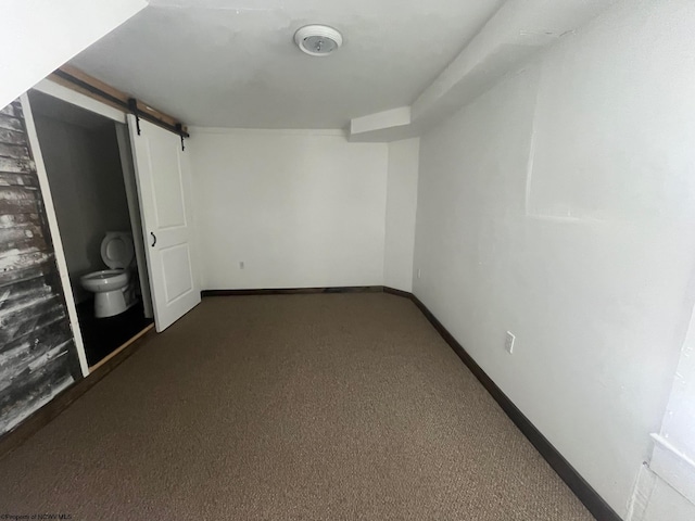 basement with a barn door and dark colored carpet