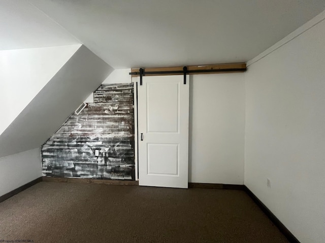 bonus room with dark carpet, a barn door, and vaulted ceiling