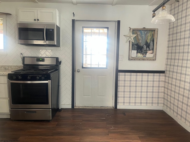 kitchen featuring white cabinetry, appliances with stainless steel finishes, dark wood-type flooring, hanging light fixtures, and light stone counters