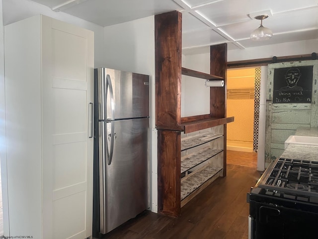 kitchen featuring tile countertops, a barn door, gas stove, dark wood-type flooring, and stainless steel refrigerator