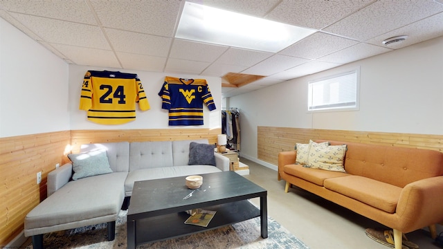 living room featuring concrete floors, a drop ceiling, and wood walls