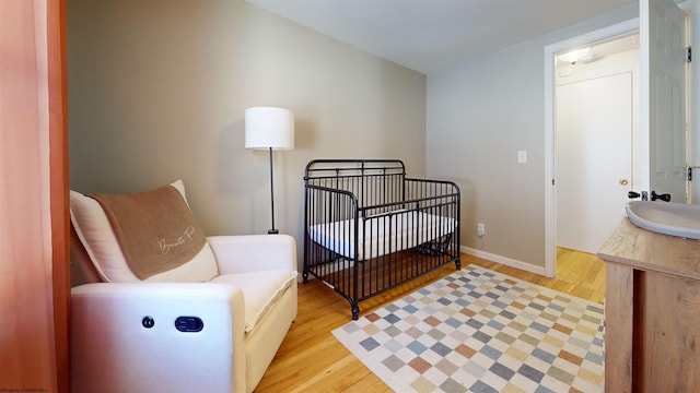 bedroom with sink, light hardwood / wood-style floors, and a crib