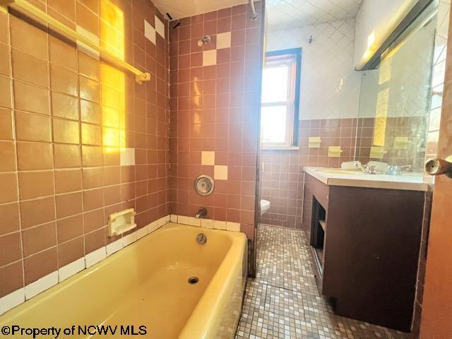 full bathroom featuring toilet, vanity, tile walls, tiled shower / bath, and tile patterned floors