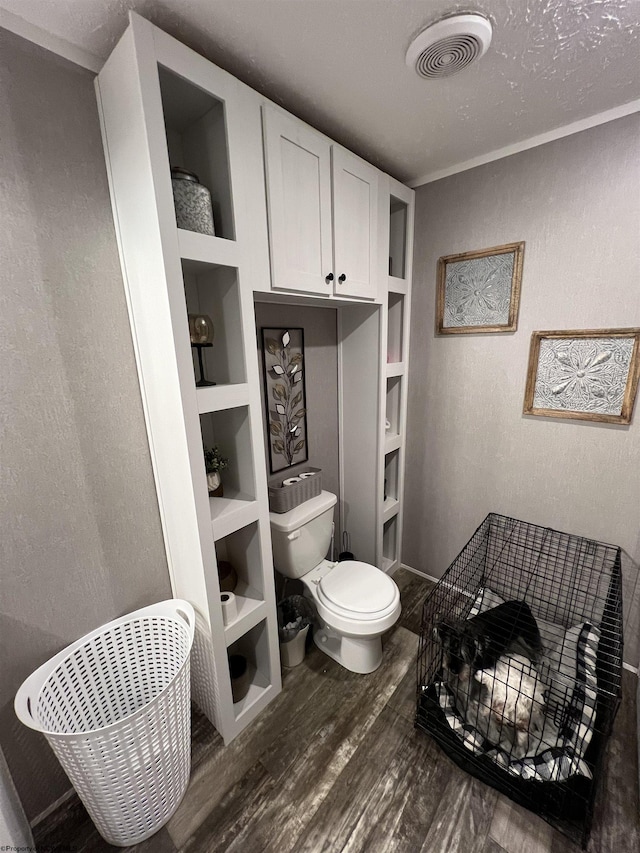 bathroom with a textured wall, toilet, wood finished floors, visible vents, and built in features