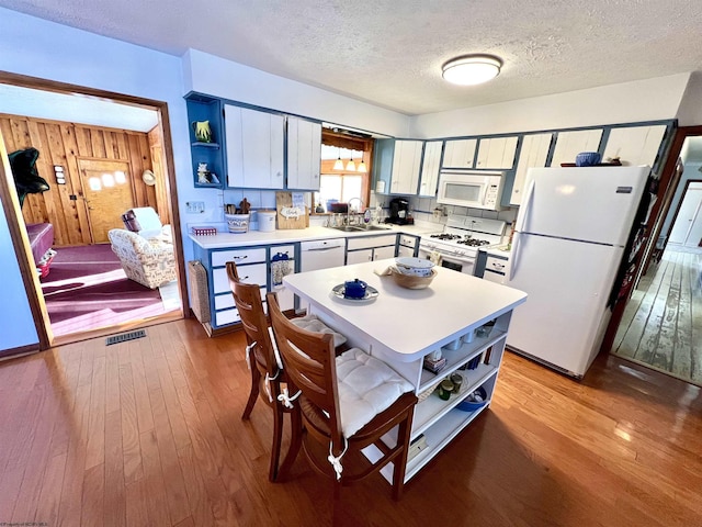 kitchen featuring white appliances, a textured ceiling, hardwood / wood-style flooring, wooden walls, and sink