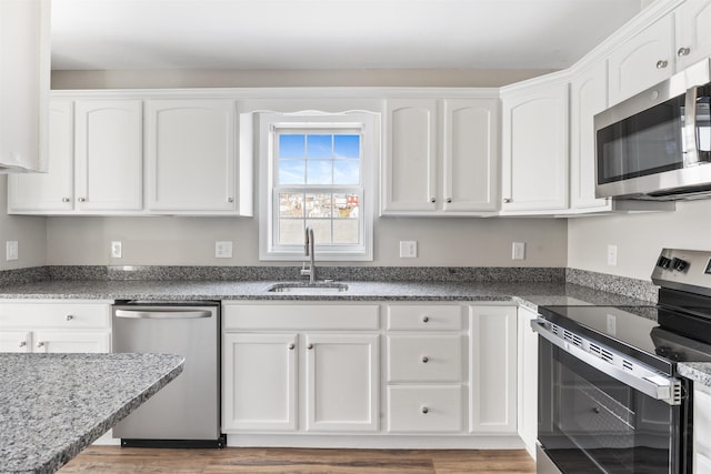 kitchen featuring appliances with stainless steel finishes, sink, hardwood / wood-style flooring, white cabinetry, and dark stone countertops