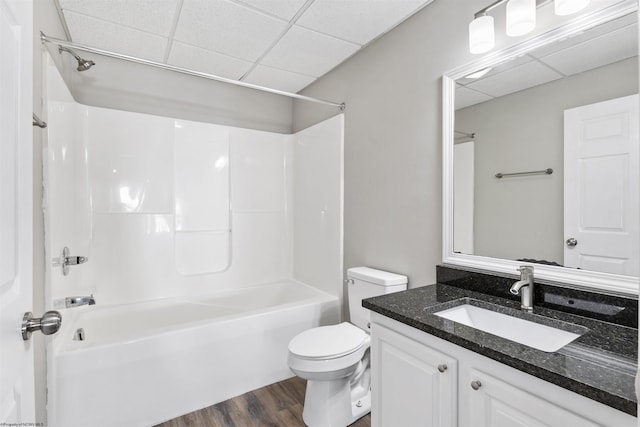 full bathroom with wood-type flooring, vanity, toilet, a drop ceiling, and bathtub / shower combination