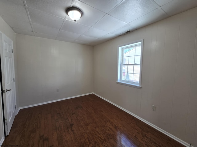 empty room featuring a drop ceiling and dark hardwood / wood-style floors