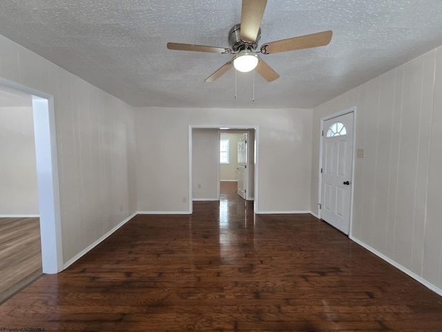 foyer entrance featuring wood walls, dark wood-type flooring, a textured ceiling, and ceiling fan