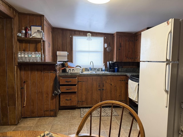 kitchen with light tile patterned flooring, wooden walls, sink, white fridge, and stove