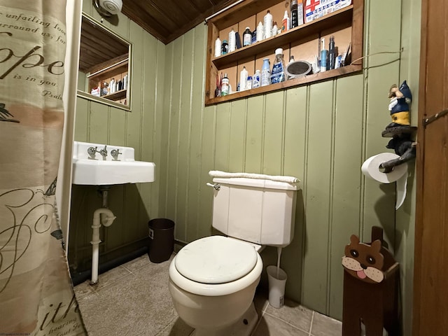 bathroom with tile patterned floors, toilet, sink, wood walls, and wood ceiling