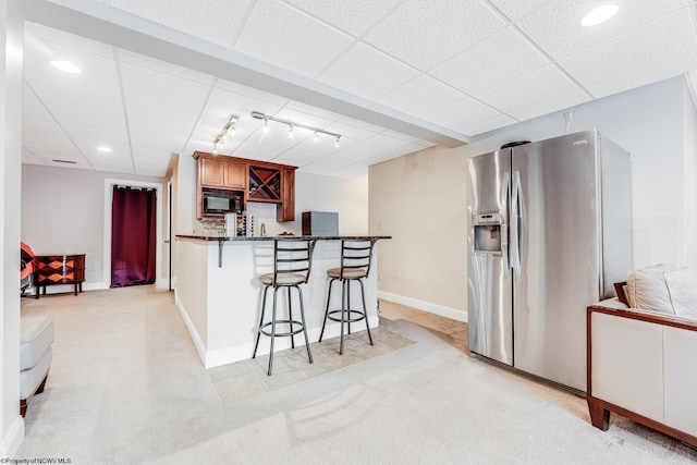 kitchen with a breakfast bar area, a drop ceiling, stainless steel fridge, and light colored carpet