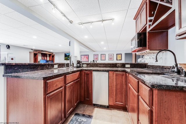 kitchen with light tile patterned floors, sink, dark stone counters, and kitchen peninsula