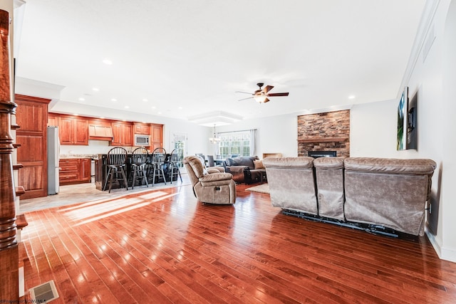 living room with hardwood / wood-style flooring, ceiling fan with notable chandelier, and a fireplace