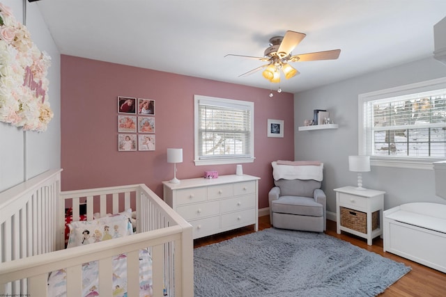 bedroom featuring wood-type flooring, a nursery area, and ceiling fan