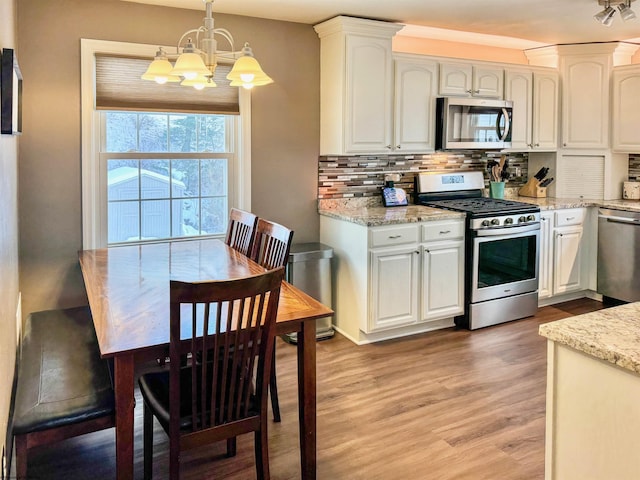 kitchen with decorative light fixtures, light wood-type flooring, appliances with stainless steel finishes, decorative backsplash, and white cabinets