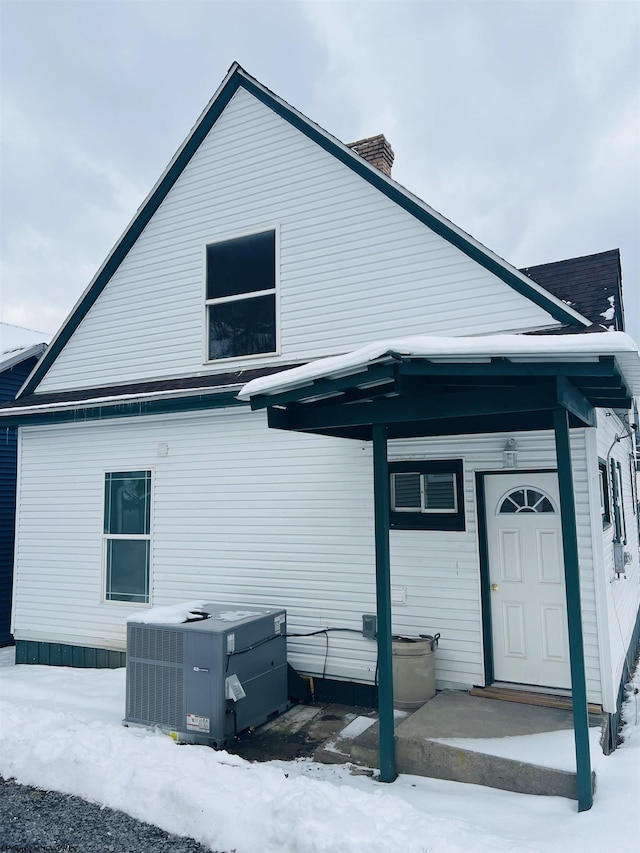 snow covered rear of property featuring central AC